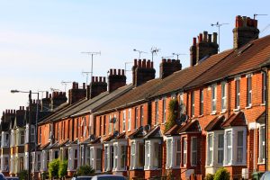 Image shows terrace semi-detached houses with red bricks and bay windows and large chimneys in a row, in day time.