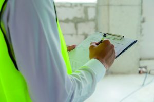foreman builder, engineer or inspector in green safety vest reflective checking and inspecting with clipboard at construction site building interior, inspection, contractor and engineering concept