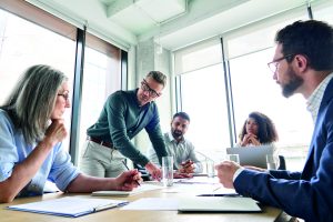 Image includes a team of five people working around a table to generate ideas. They have notebooks in front of them
