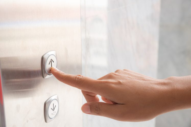 Woman's hand pressing the 'up' elevator button - pic: Shutterstock / siam.pukkato