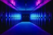 A symmetrical corridor inside a data centre, lined with rows of server racks on both sides, illuminated by blue and purple lighting.