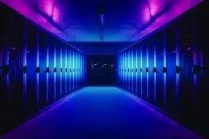 A symmetrical corridor inside a data centre, lined with rows of server racks on both sides, illuminated by blue and purple lighting.