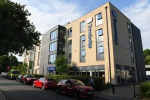 Image shows exterior of modern hotel, let by Travelodge with cars parked outside.