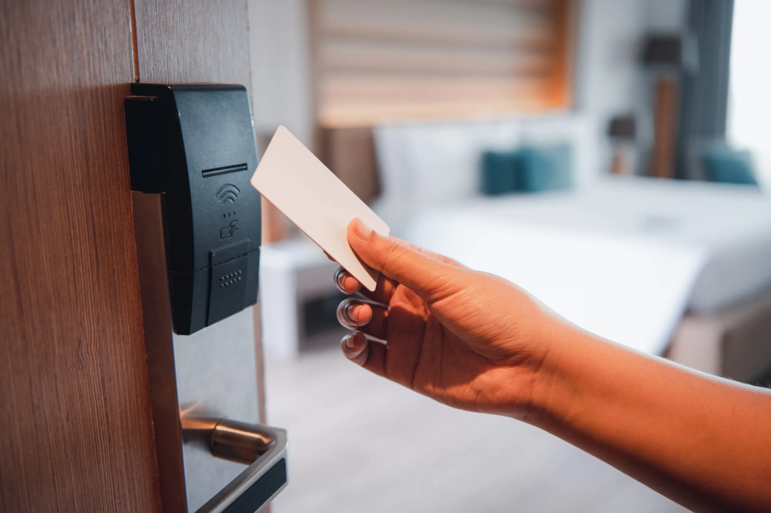 Photo shows hotel door ajar as somebody uses their electronic car key to enter. In the background, a white bed can be seen